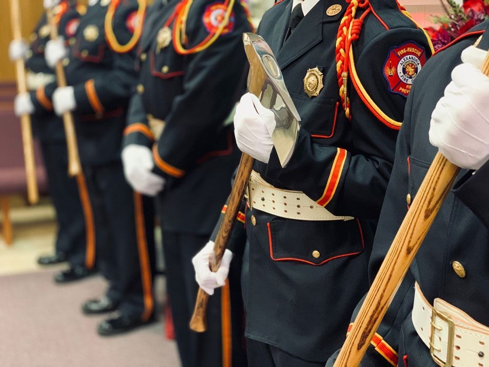 Uniformed honor guard members holding rifles in formation, black and red uniforms with white gloves