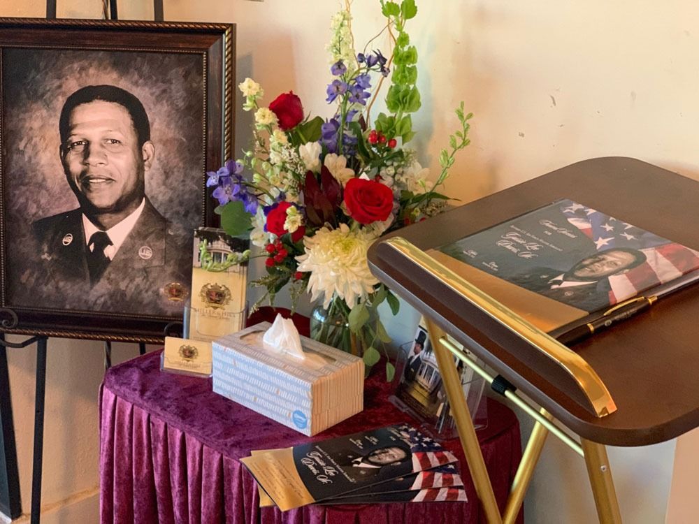 Memorial display with framed portrait, flowers, and books on a purple-draped table