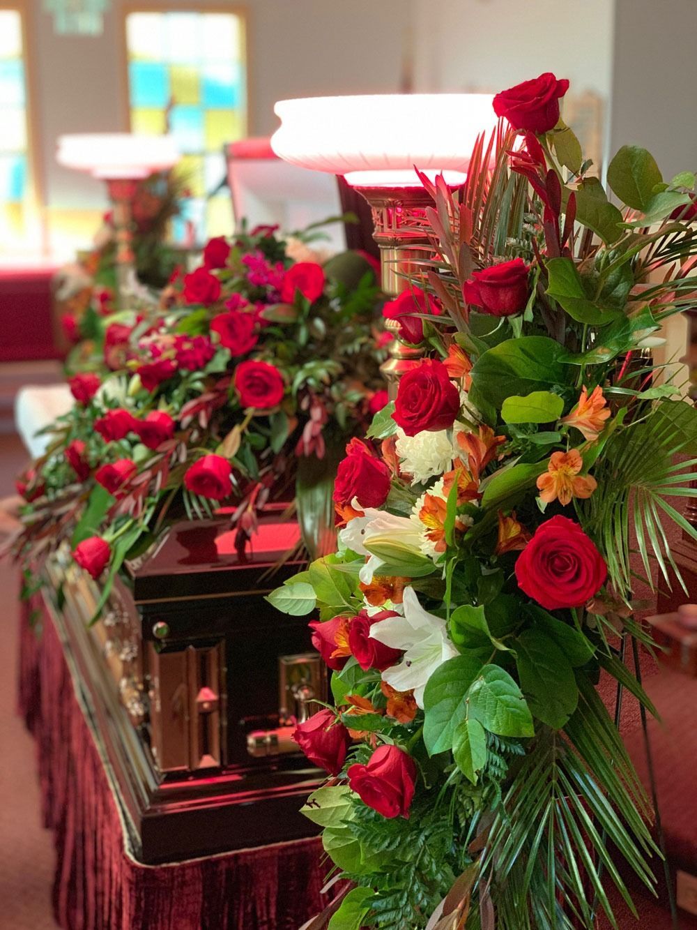 Red and white funeral flowers arranged around a casket in a chapel