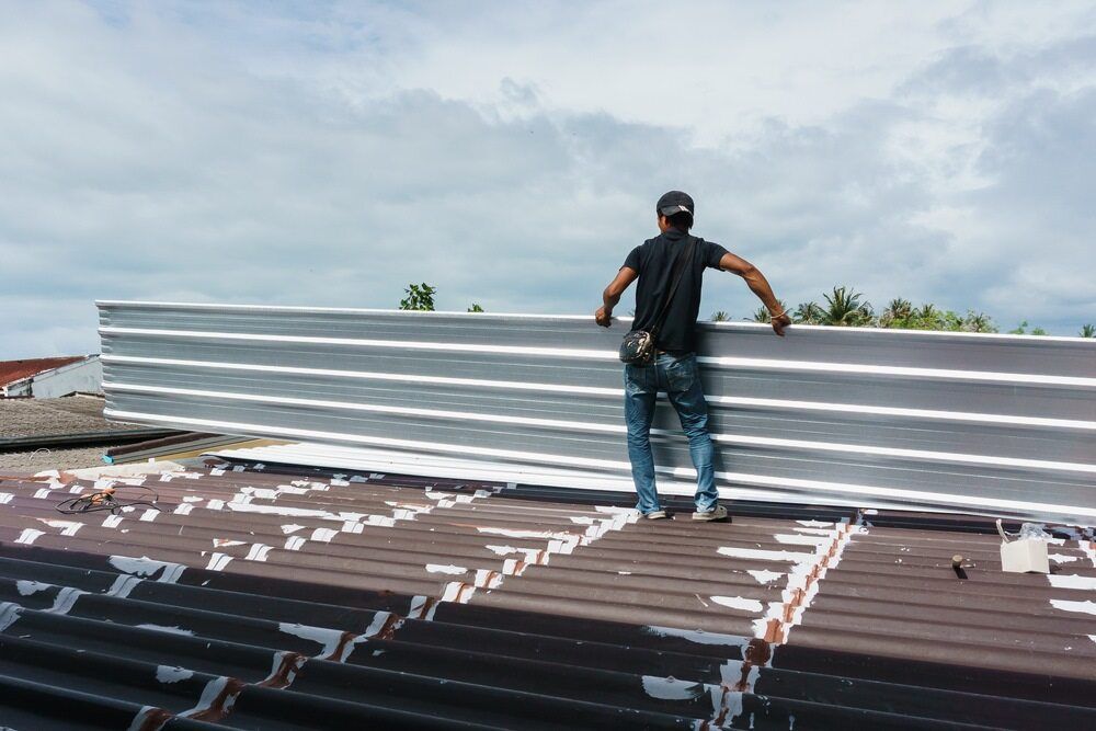 A Man is Standing on Top of a Roof Holding a Piece of Metal — Accurate Fitout Solutions In Wetherill Park, NSW