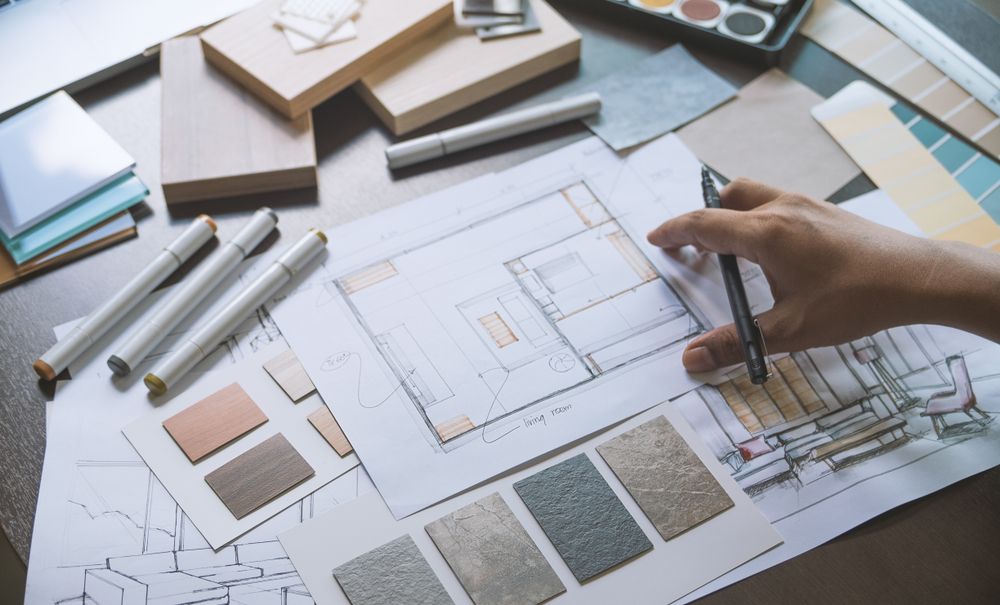 Someone is holding a pen over a desk strewn with design documents — The Right Kitchen Company in Thirroul, NSW