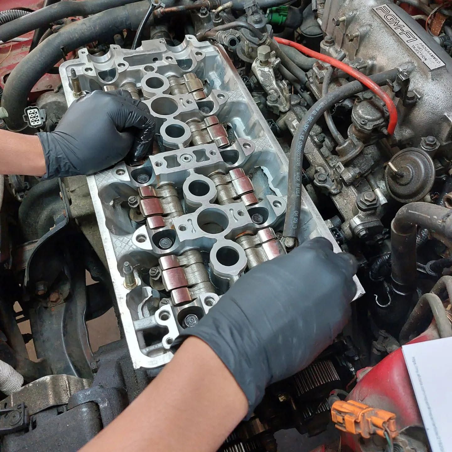 Hands working on a car engine, removing a cylinder head in a garage. | VP Automotive LLC