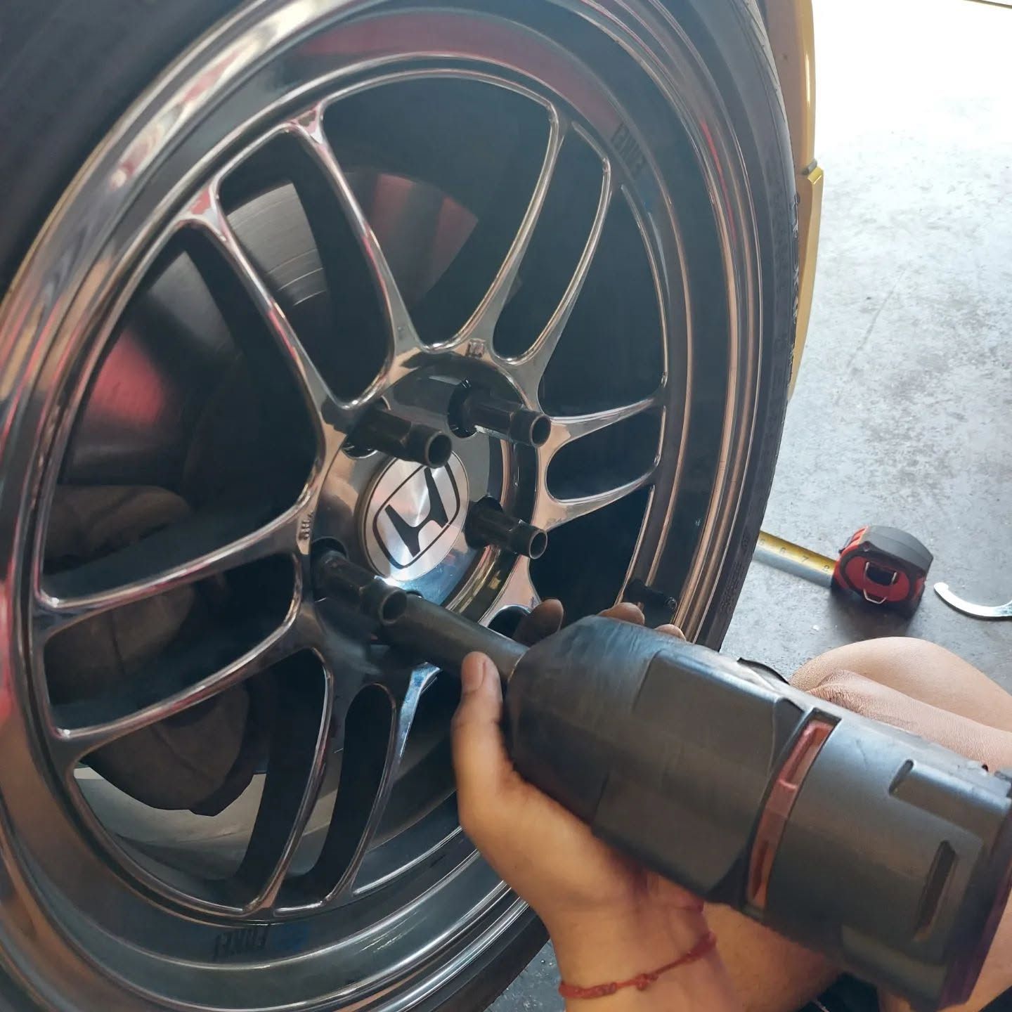 Hand using a power tool to tighten a black car wheel lug nut in a garage | VP Automotive LLC