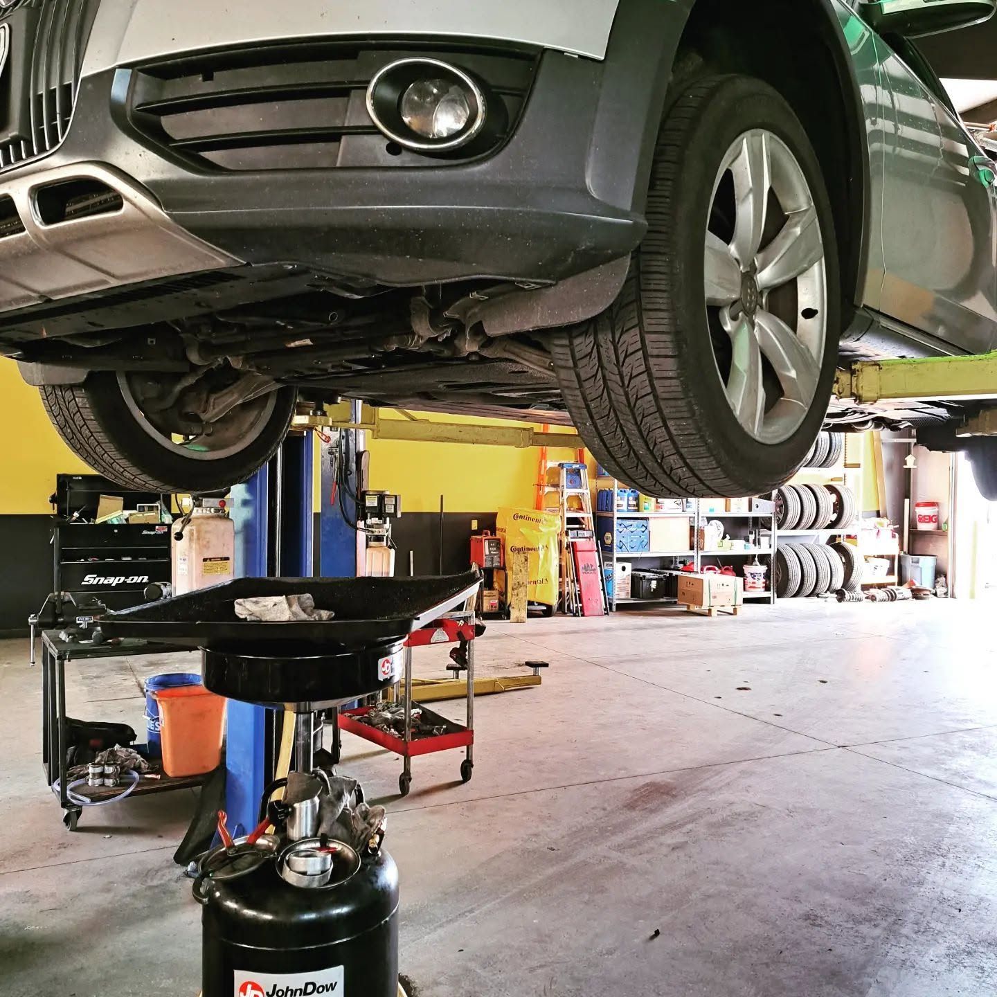 Car on a lift over an oil drain pan in a garage with tools and tires nearby | VP Automotive LLC