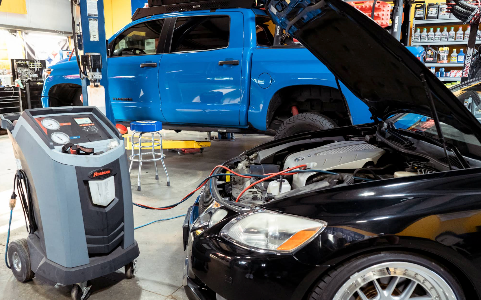 Auto repair shop with a blue SUV on a lift and a black car under a hooded inspection machine | VP Automotive LLC
