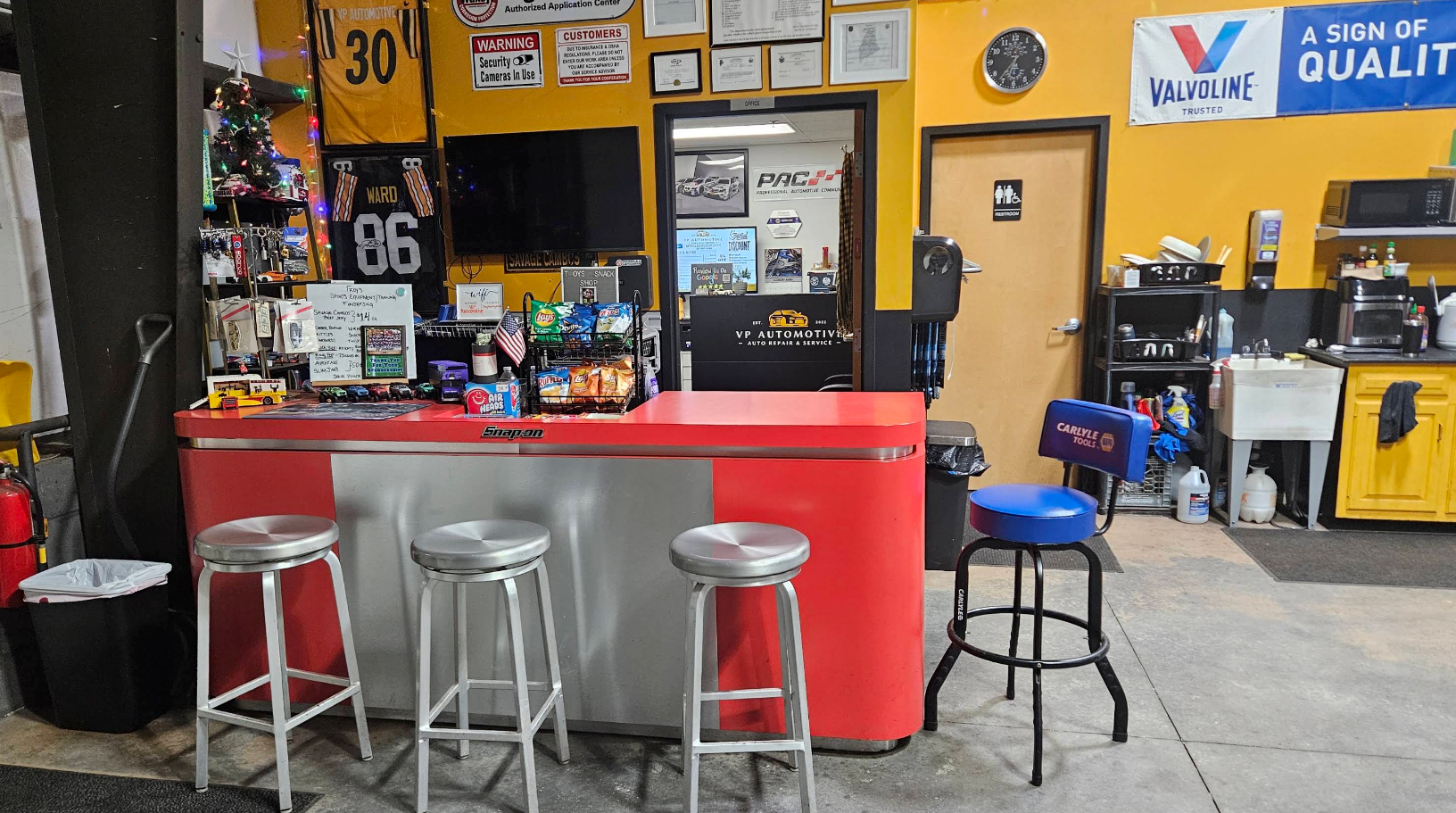 Auto shop counter with red front, metal stools, and yellow-black wall signs | VP Automotive LLC