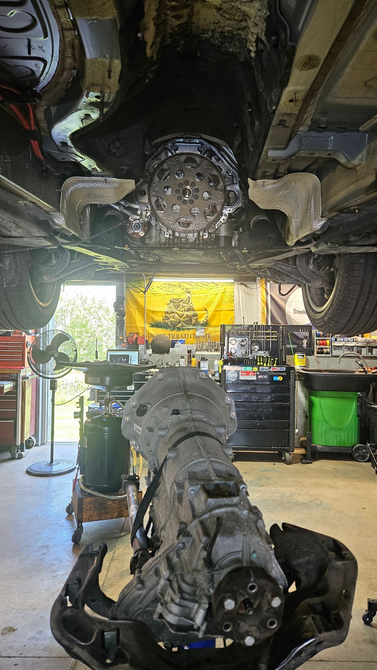 Undercarriage of a vehicle in a garage, with a detached axle or drivetrain on the floor beneath | VP Automotive LLC