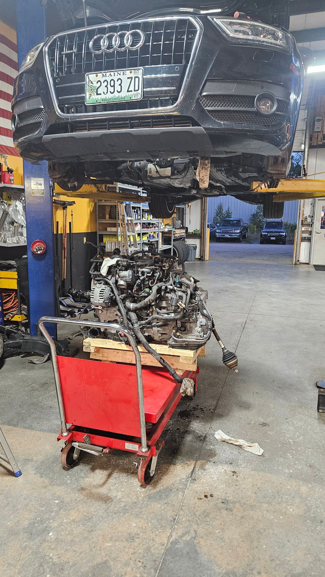 Car lifted on a repair bay with a detached engine on a red cart in an auto shop | VP Automotive LLC