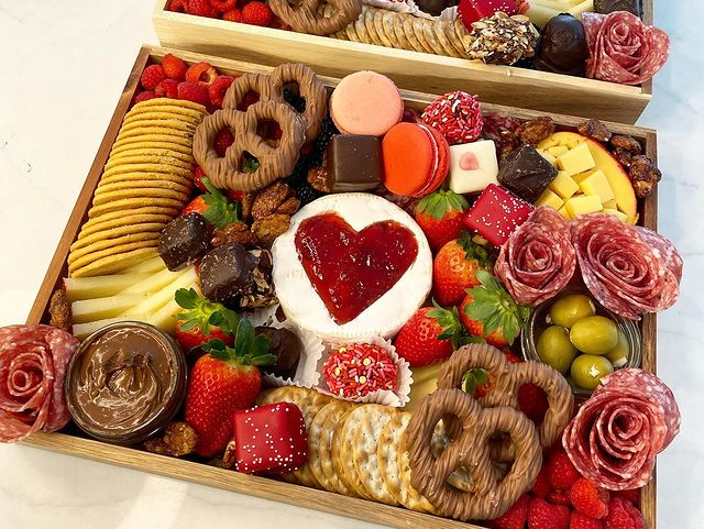 A wooden tray filled with a variety of food and a heart shaped marshmallow.