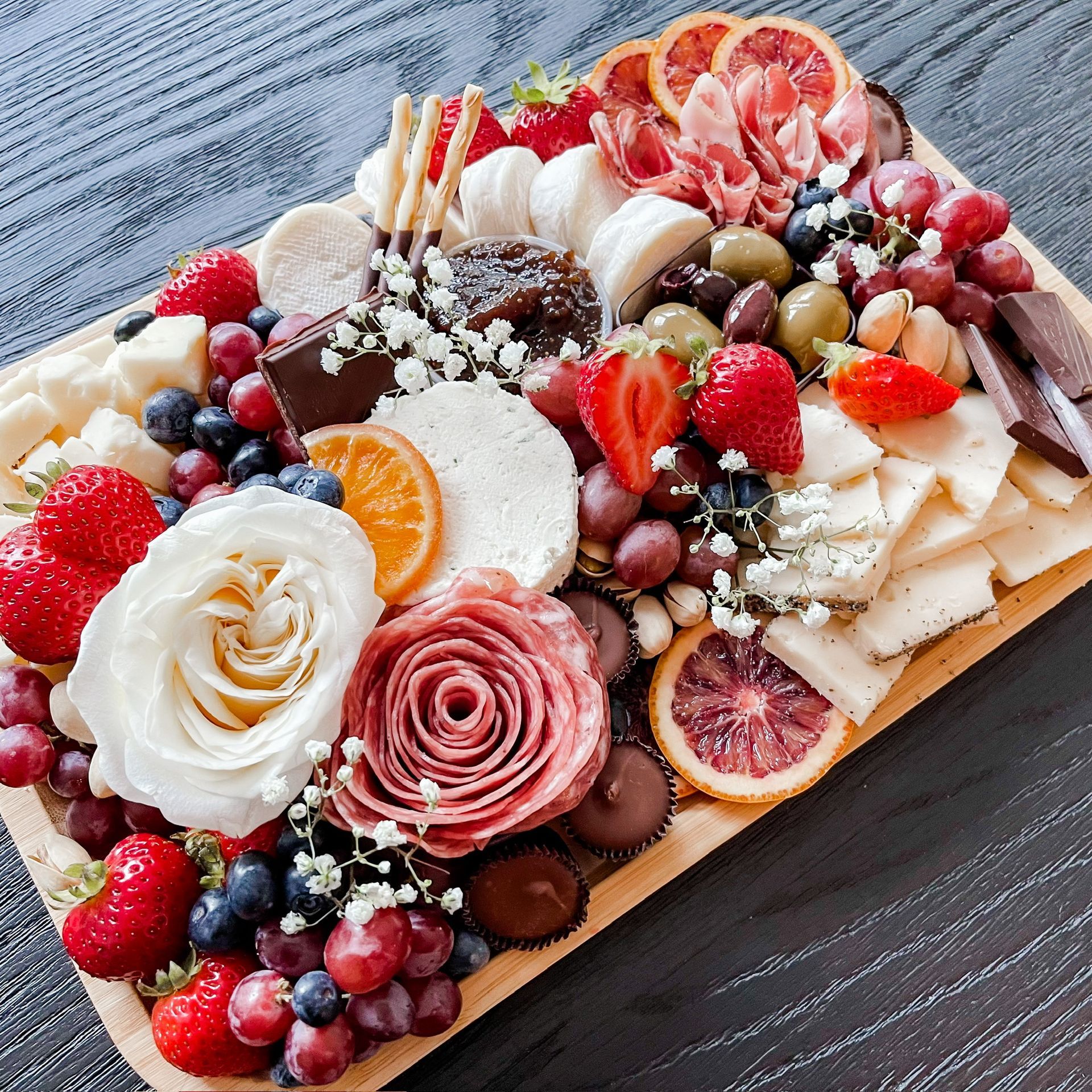 A wooden cutting board filled with fruits , cheeses , and flowers.