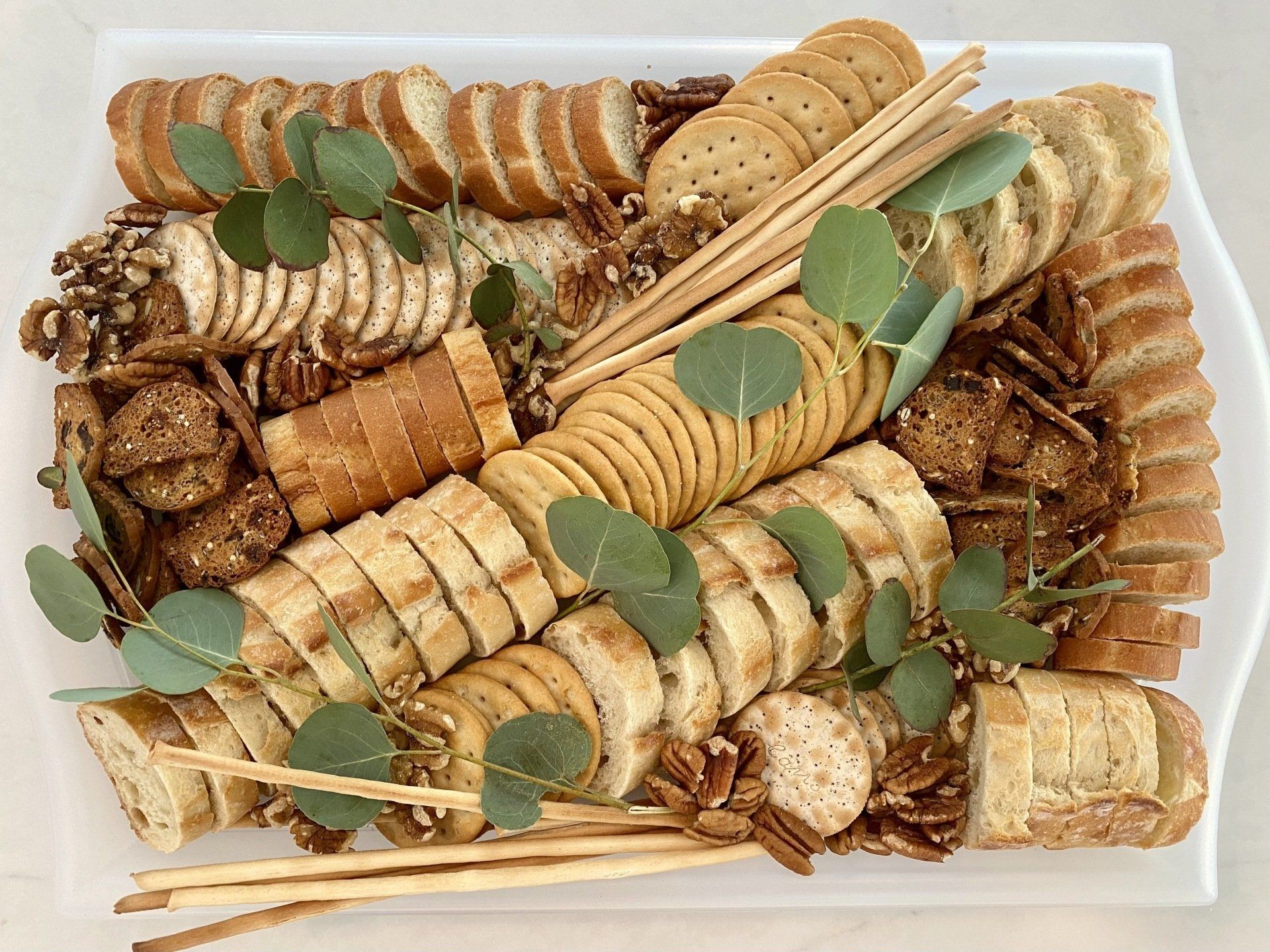 A white tray filled with bread , crackers , and nuts.