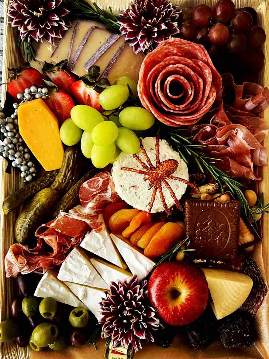 A wooden tray filled with meats , cheeses , fruits and flowers.