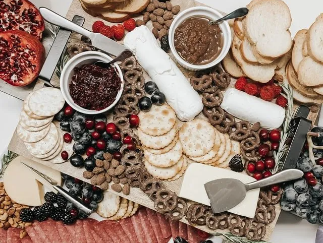 A cutting board filled with crackers , cheese , berries , and nuts.