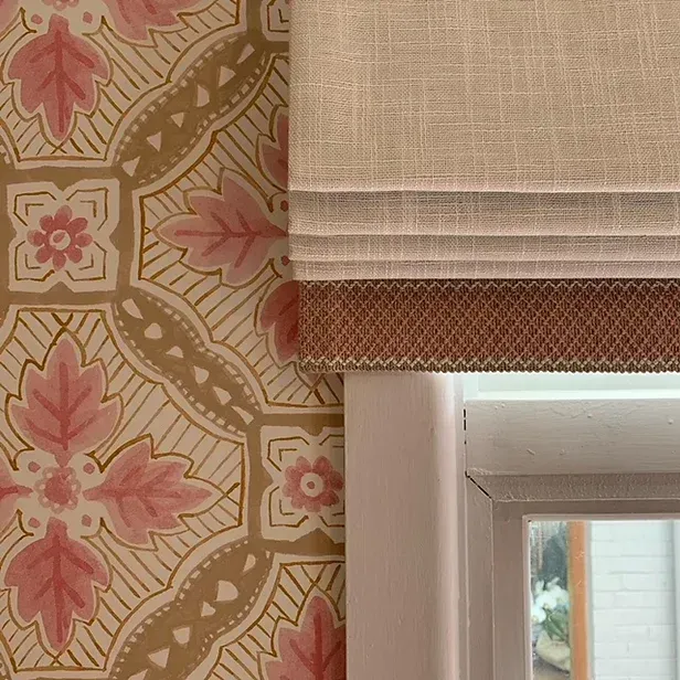 A window with a roman shade on it next to a wall with pink flowers on it.