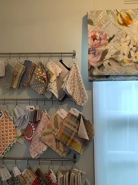 A bunch of fabrics are hanging on a rack next to a window.