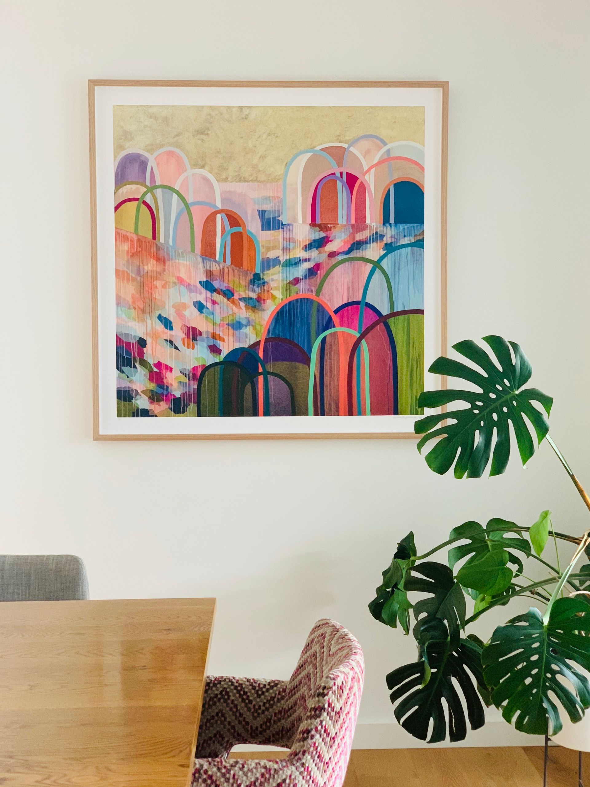 A living room with a desk , chairs , plants and a clock on the wall.
