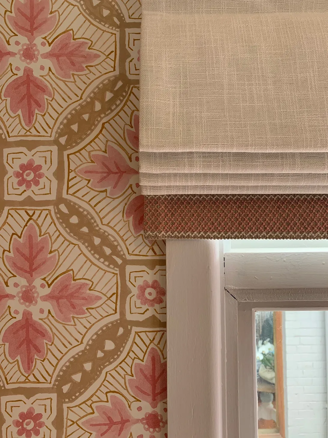 A window with a floral wallpaper and a roman shade