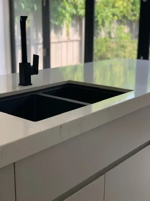 A kitchen sink with a black faucet on a white counter top.