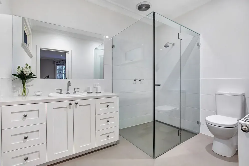 A bathroom with a walk in shower, toilet, sink and mirror.