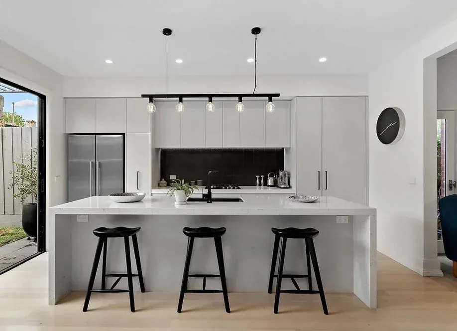 A kitchen with white cabinets and black stools and a large island.