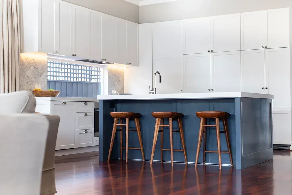 A kitchen with white cabinets and a blue island with wooden stools.