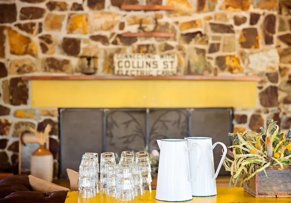 A table with glasses and pitchers on it in front of a stone fireplace.