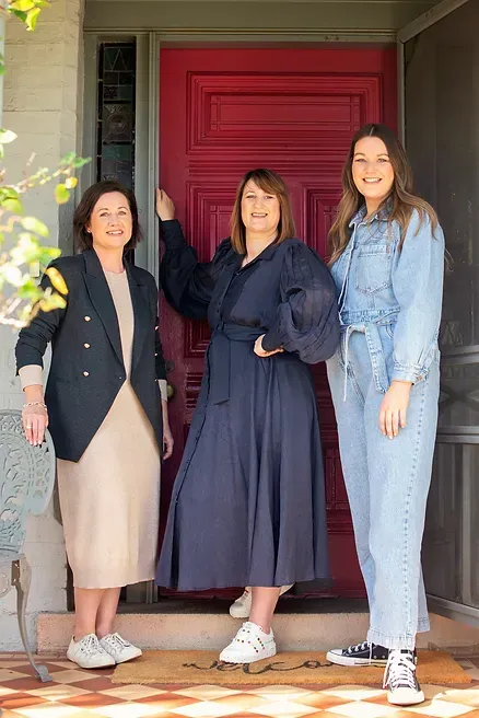 Three women are standing in front of a red door.