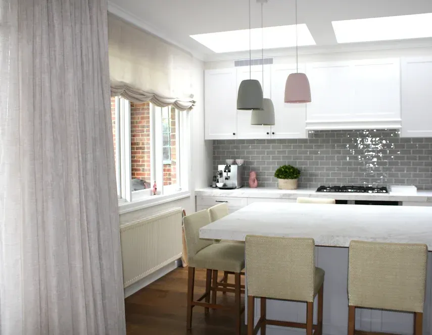 A kitchen with white cabinets, stools, a stove and a window.