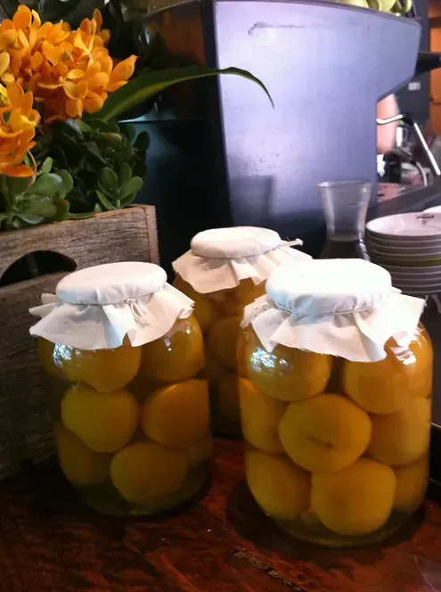 Three jars of pickled lemons on a table with flowers in the background