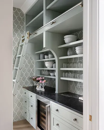 A pantry with a ladder and shelves filled with bowls and glasses.