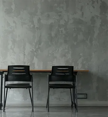 Two black chairs are sitting next to a wooden table in front of a concrete wall.