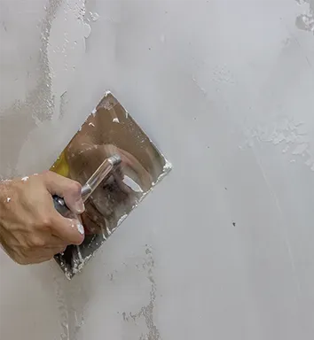 A person is plastering a wall with a trowel.