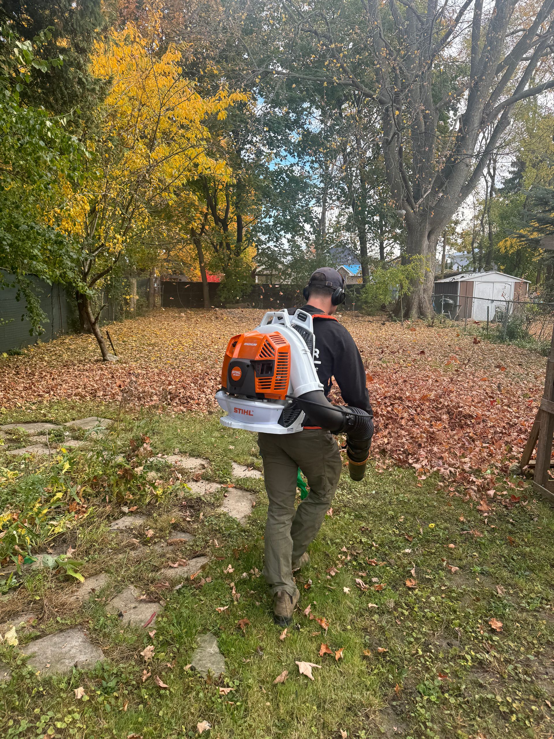 A man is carrying a leaf blower on his back in a yard.