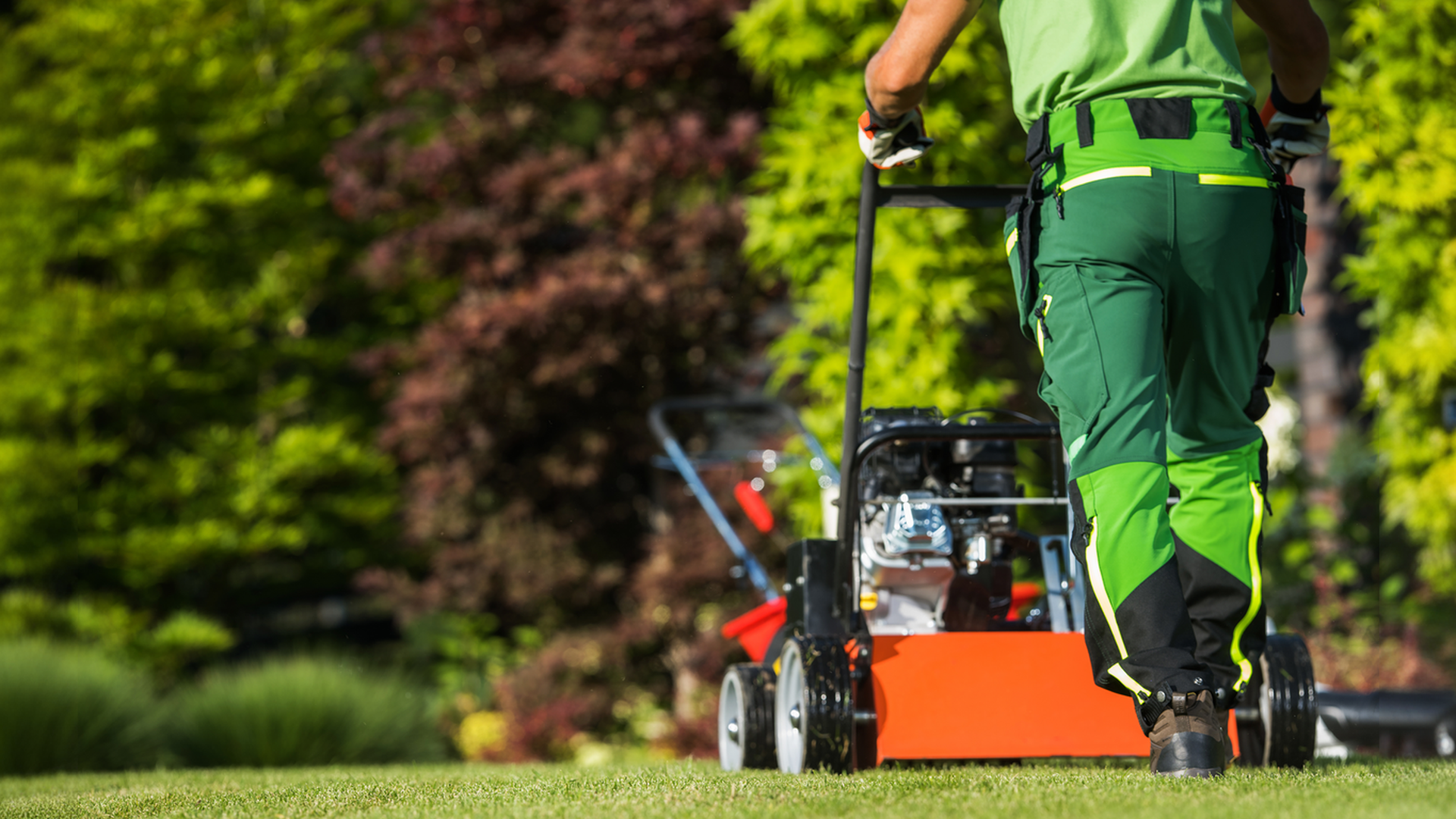 A man is pushing a lawn mower on a lush green lawn.