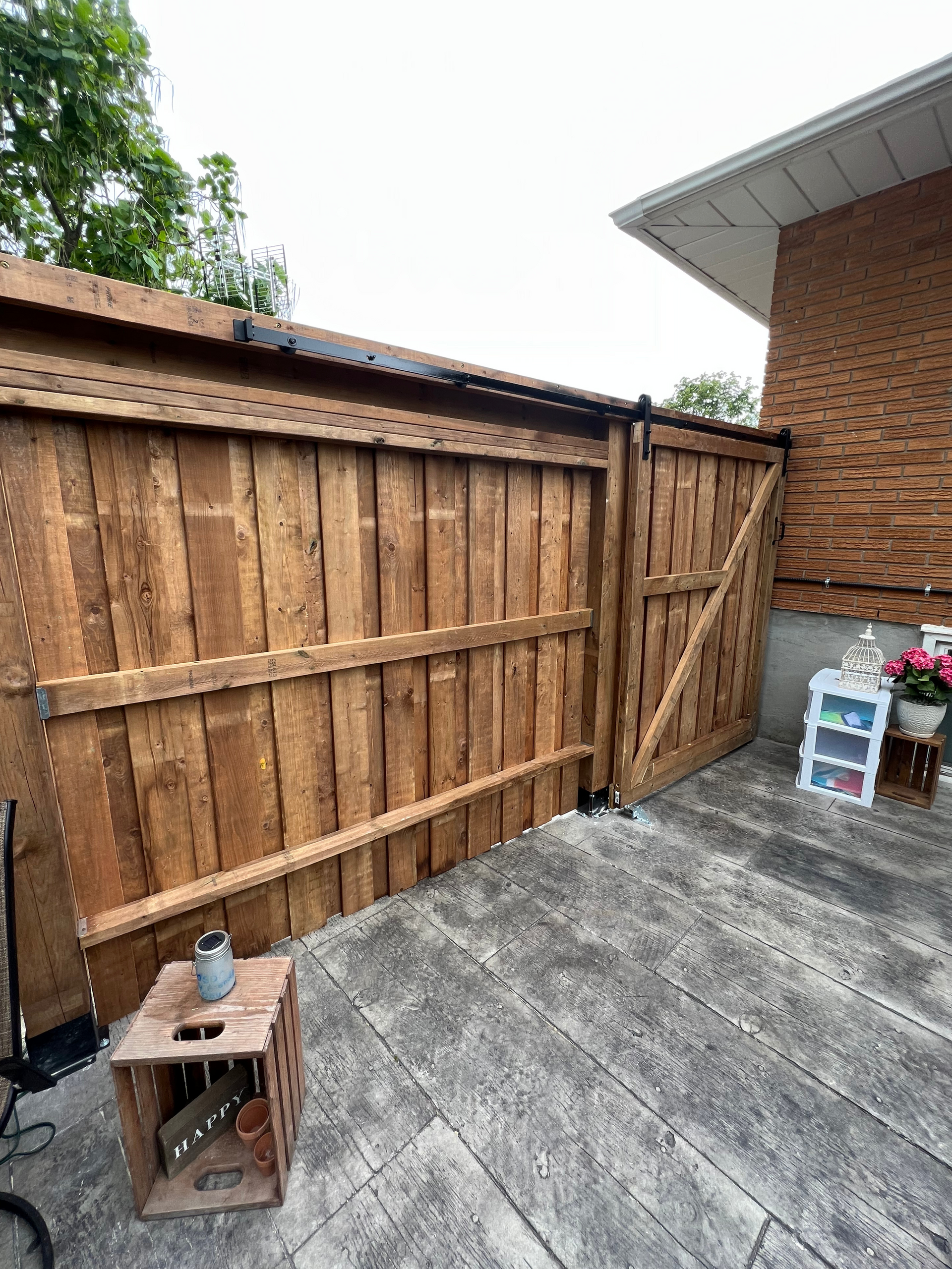 A wooden fence is sitting on top of a wooden deck next to a brick building.