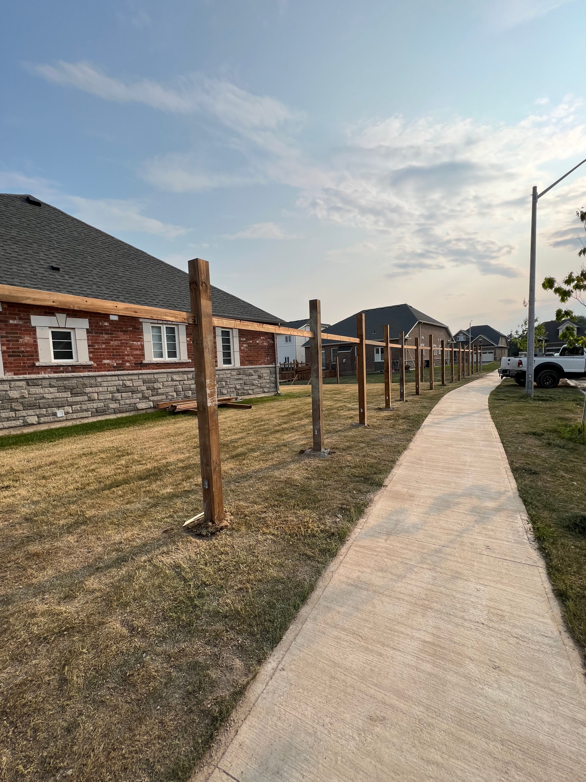 A wooden fence is being built next to a sidewalk in front of a house.