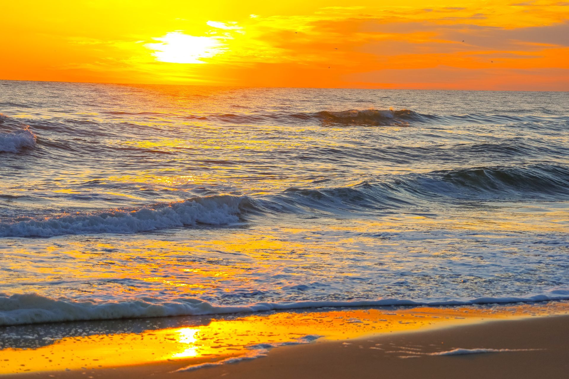 Golden sunset reflecting on ocean waves crashing onto a sandy beach.