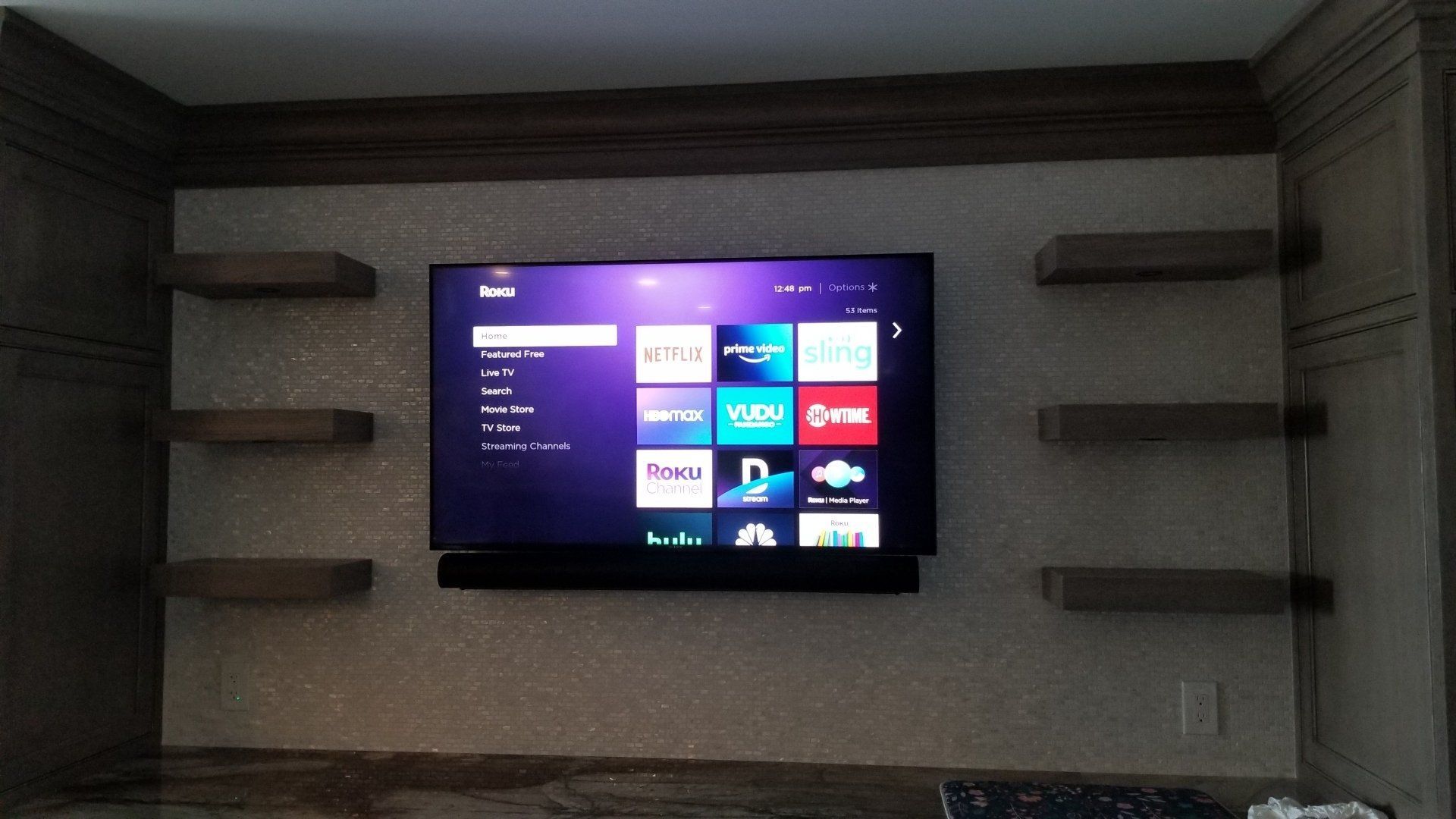 A TV and soundbar are custom mounted on a ceramic tile wall for a bar by fisher custom av.