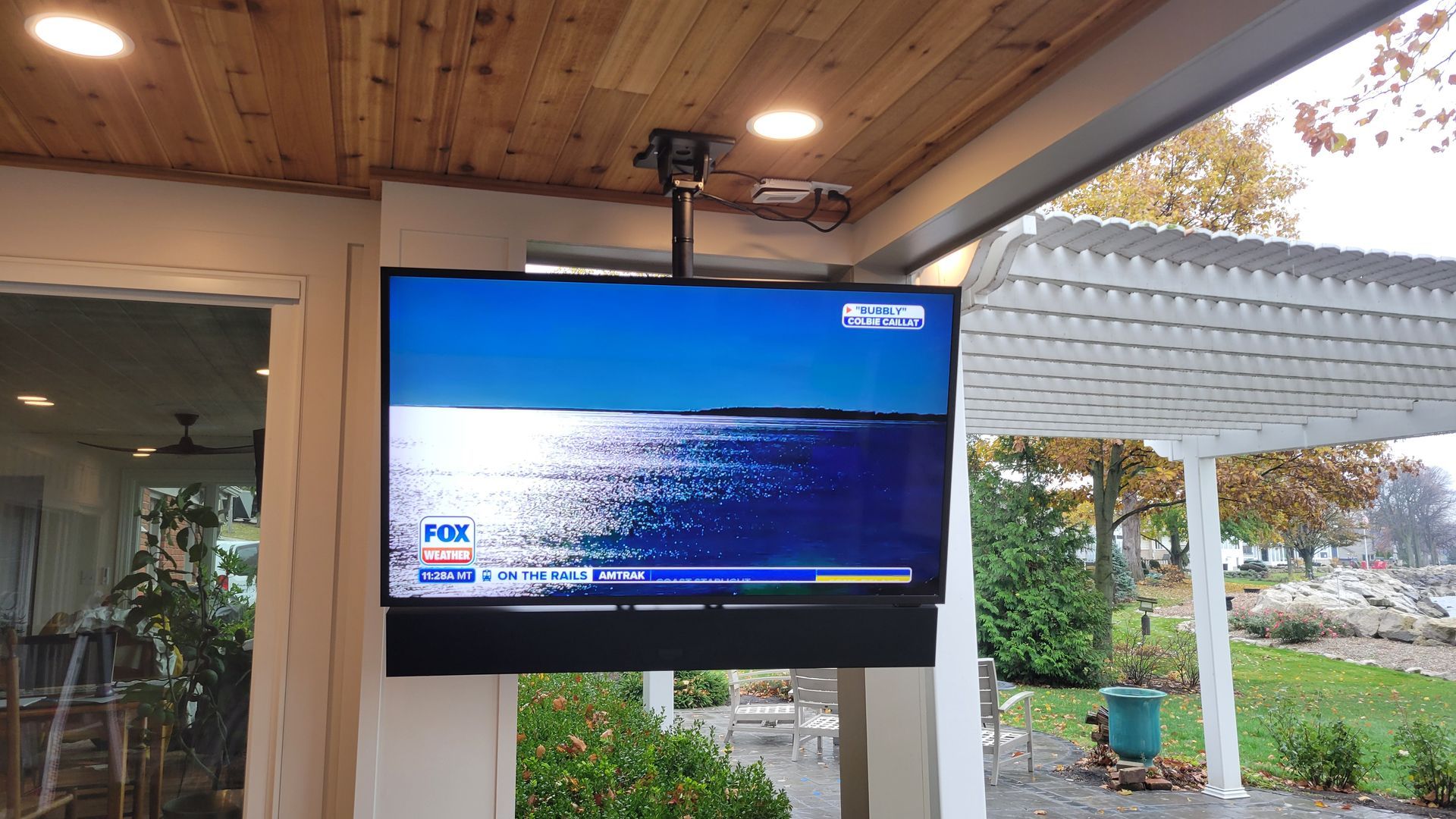 Weatherproof outdoor TV mounted on pillar by fisher custom av overlooking backyard water feature.