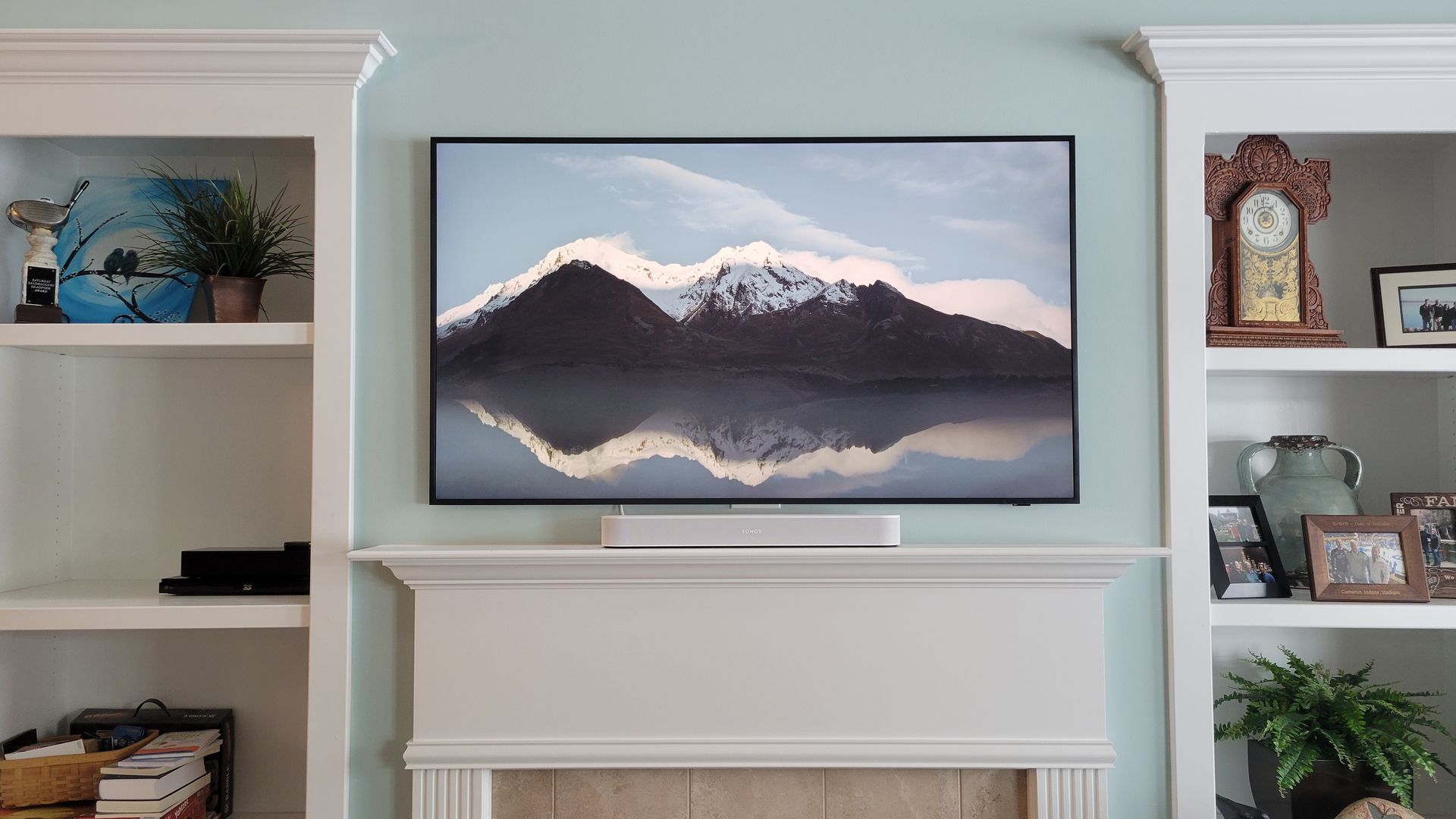 Built-in shelves with a samsung frame TV and soundbar mounted above a fireplace.