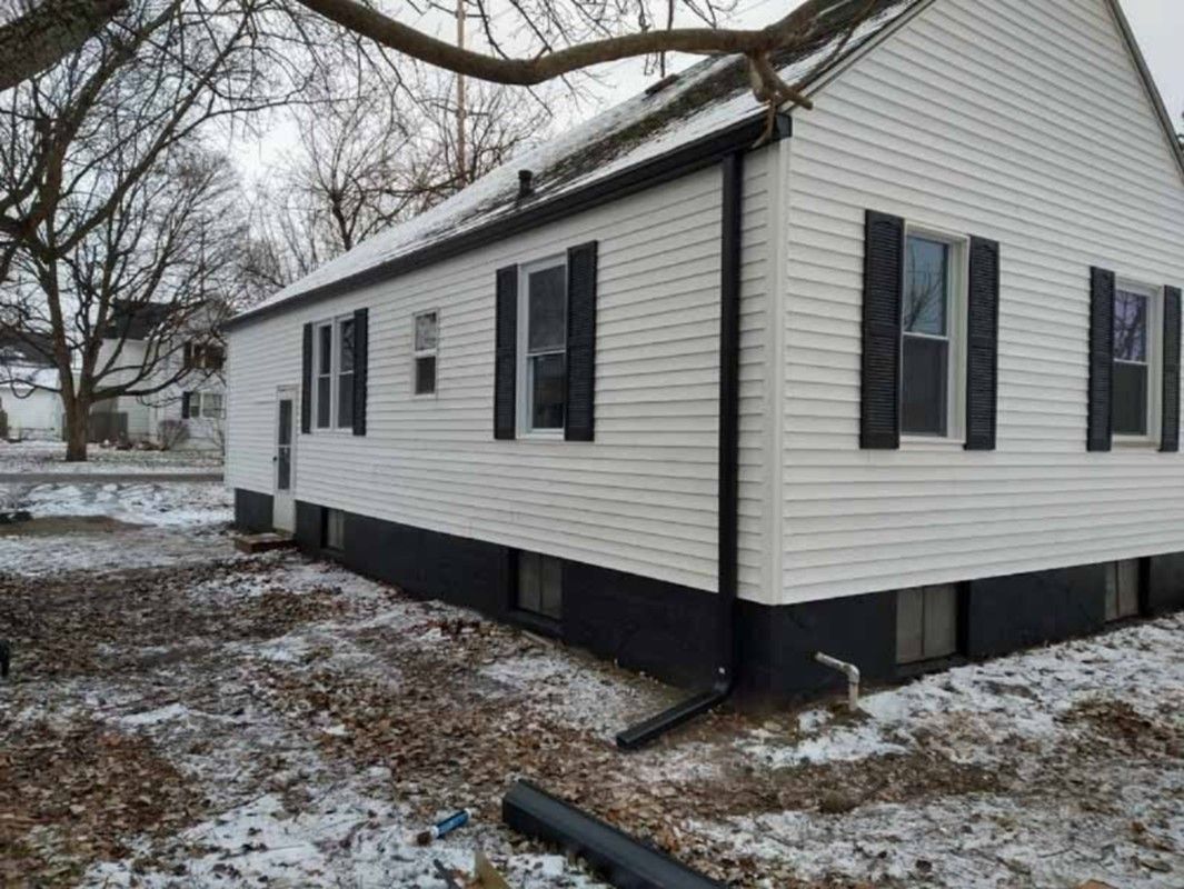 White single-story house with vinyl siding and black shutters in a snowy yard.