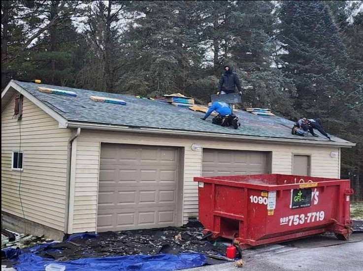 Three workers installing or repairing a shingled roof on a beige garage with two large garage doors. Three workers installing or repairing a shingled roof on a beige garage with two large garage doors.