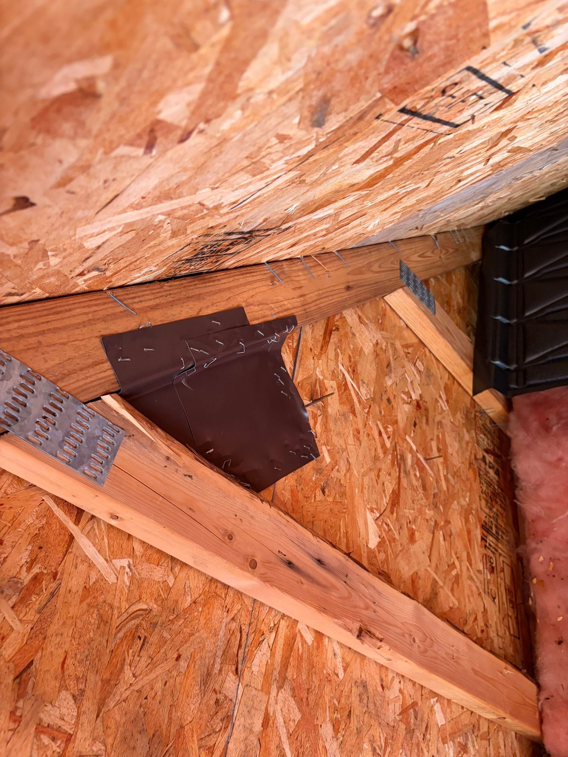 Wooden attic framing with OSB sheathing and a dark metal flashing detail near a vent opening