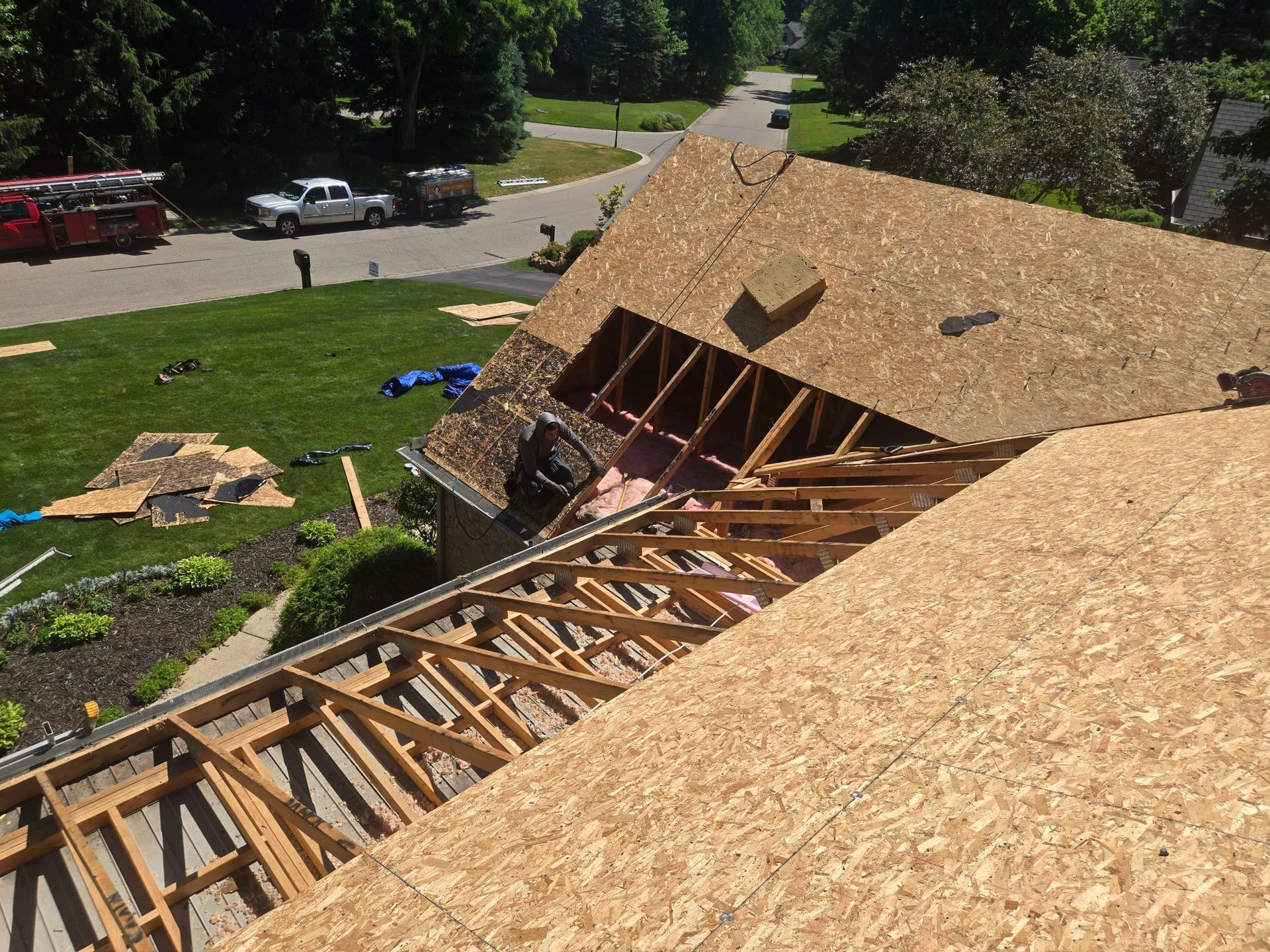 Collapsed house roof with exposed wooden trusses and debris in a grassy suburban yard