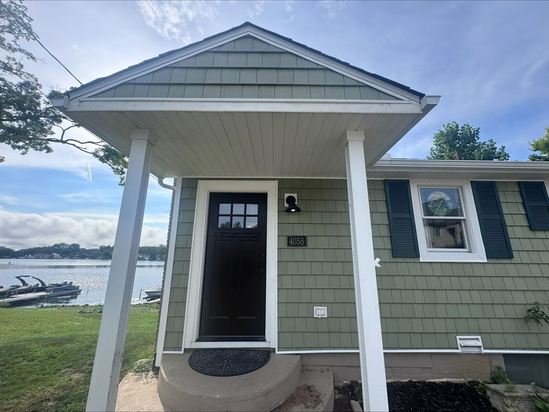 House exterior with newly installed green siding and white trim near a lakeside view. House exterior with newly installed green siding and white trim near a lakeside view.