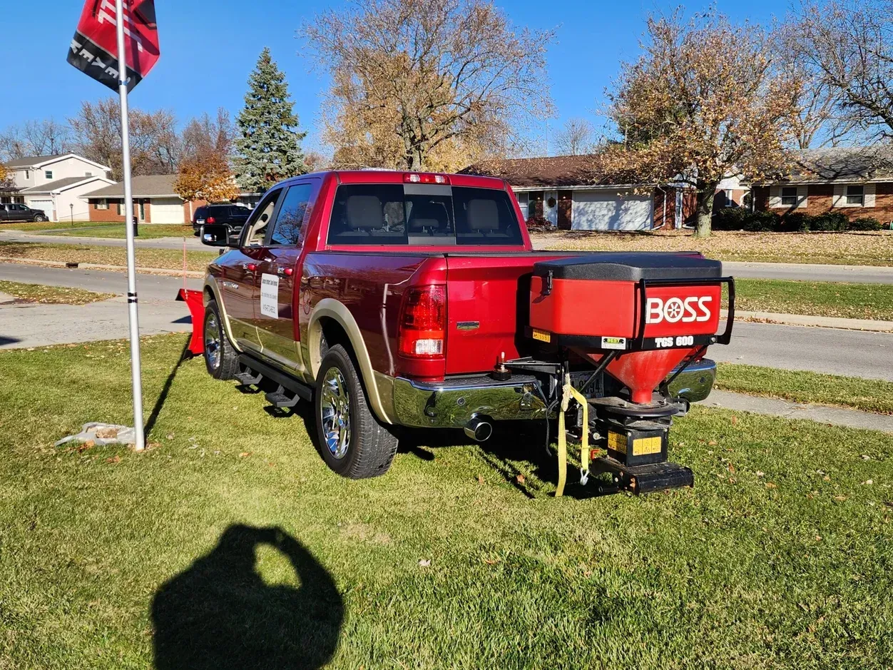 Red pickup truck with a BOSS snow plow parked on grass beside a street on a sunny day