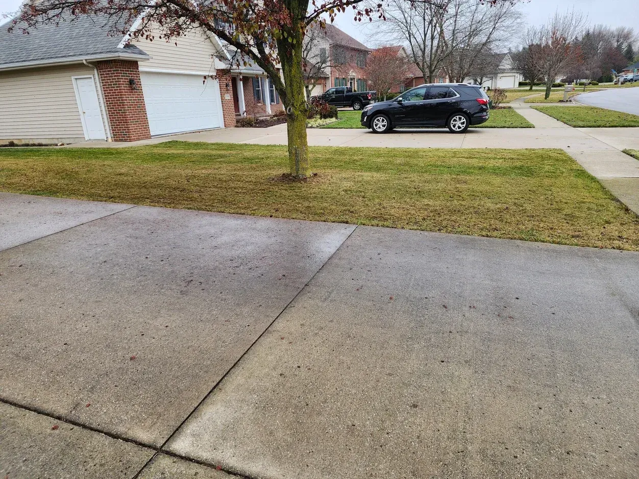 Suburban driveway and lawn with a black car parked by a brick house on a cloudy day