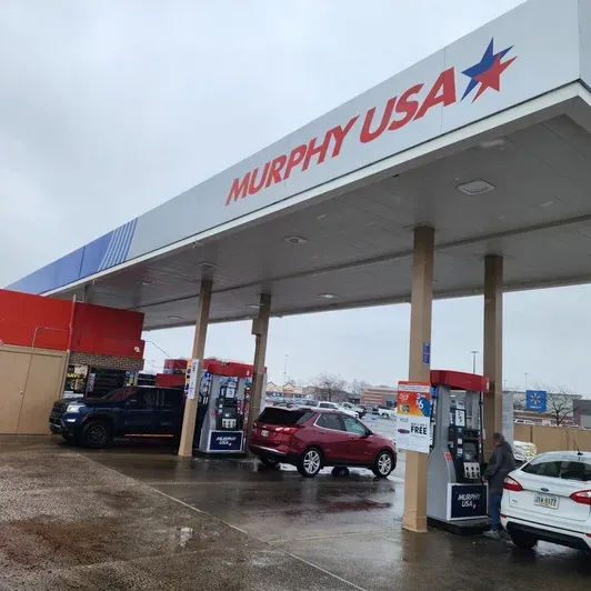 Murphy USA gas station canopy with cars fueling at pumps on a wet, overcast day