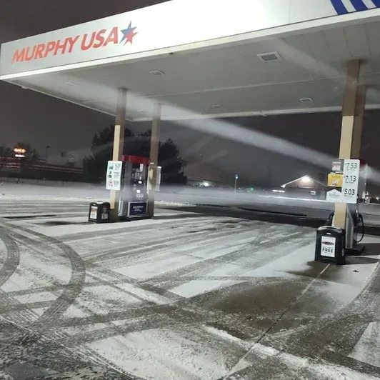 Snowy Murphy USA gas station at night with empty pumps and tire tracks in the lot
