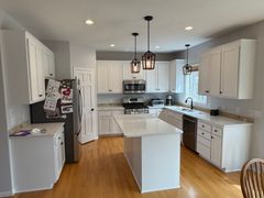 Bright white kitchen with island, stainless appliances, wood floors, and pendant lights